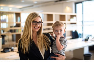 Blonde Frau im Büro mit kleinem Kind auf dem Arm